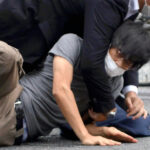 Tetsuya Yamagami, bottom, is detained near the site of gunshots in Nara Prefecture, western Japan, Friday, July 8, 2022.